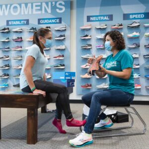 running well employee showing a customer how to assess the tread of a running shoe