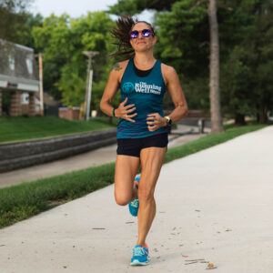 woman wearing a tank top displaying the running well store logo running outdoors