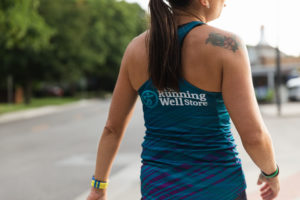 woman wearing a tank top displaying the running well store logo outdoors