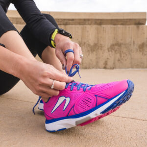 woman sitting on ground tying shoelaces of running shoes