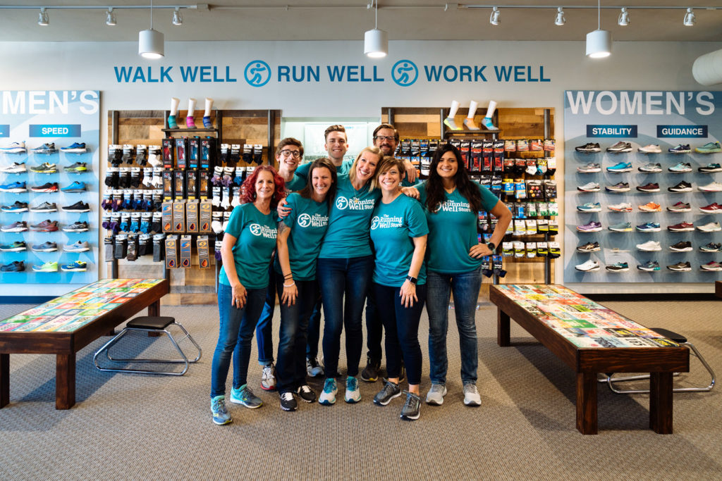 group of fit gurus at the running well store wearing gear and standing in front of running socks and running shoes