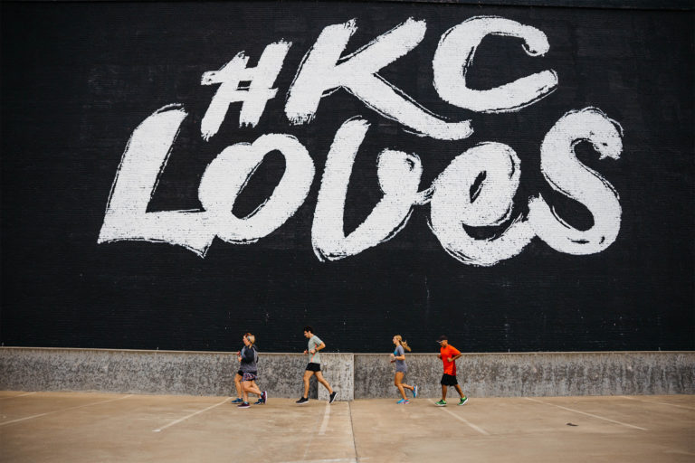 group of runners jogging in front of a kansas city mural